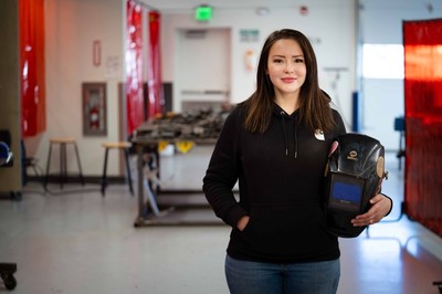 A woman holding a welding mask poses for a photo.